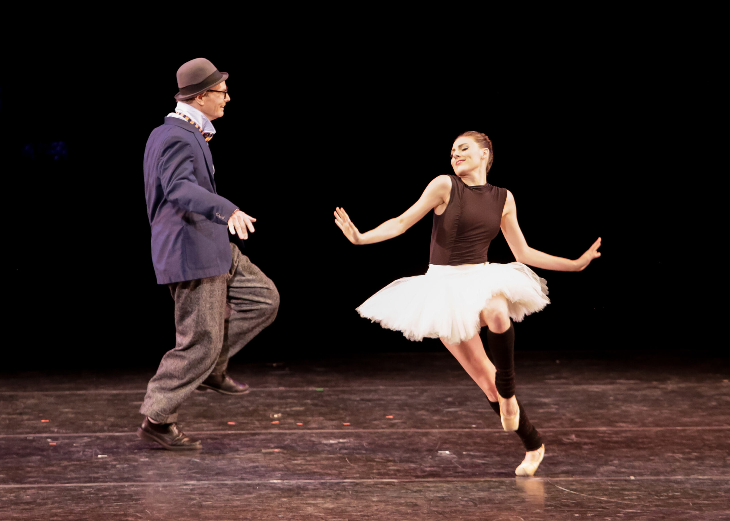 Bill Irwin is caught in profile, his knees bent and one foot rising from the floor, hands lightly extended to the side as though for balance. Slightly downstage, Tiler Peck prances through a similar movement, shoulders shrugged and a delighted smile on her face.