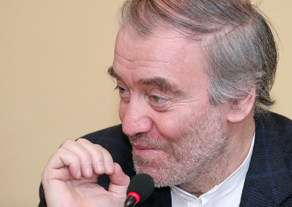 Valerie Gergiev, in a suit, speaking with his hand near his mouth. He has gray hair and a gray beard.