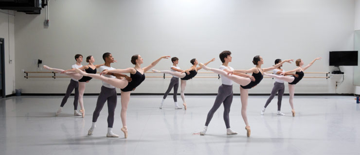 Students in a ballet student standing in partnered pique arabesques