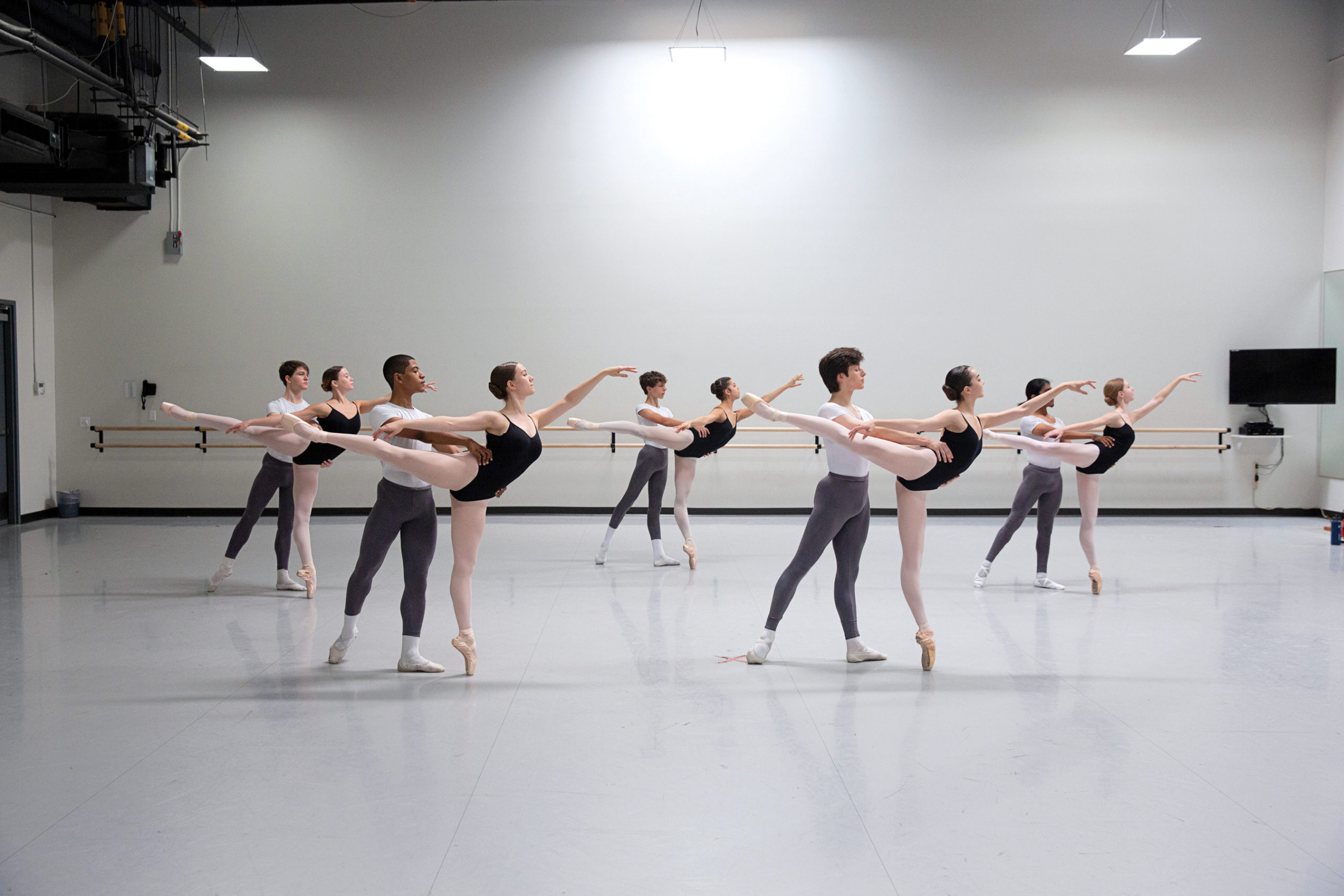Students in a ballet student standing in partnered pique arabesques