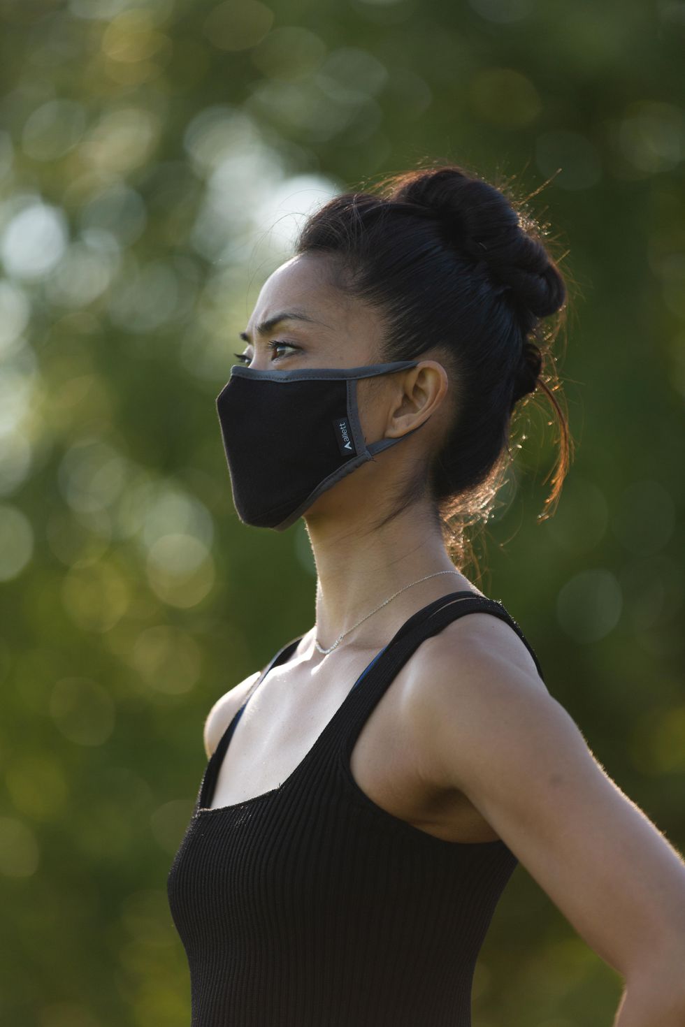 Stella Abrera stands tall in a black mask and black tank top, hair in a messy bun
