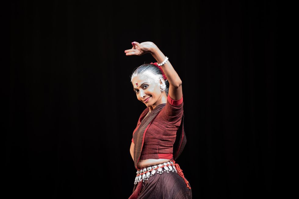 Bijayini Satpathy smiles slyly while performing, looking up from under her raised arm with pinky and thumb pressed together