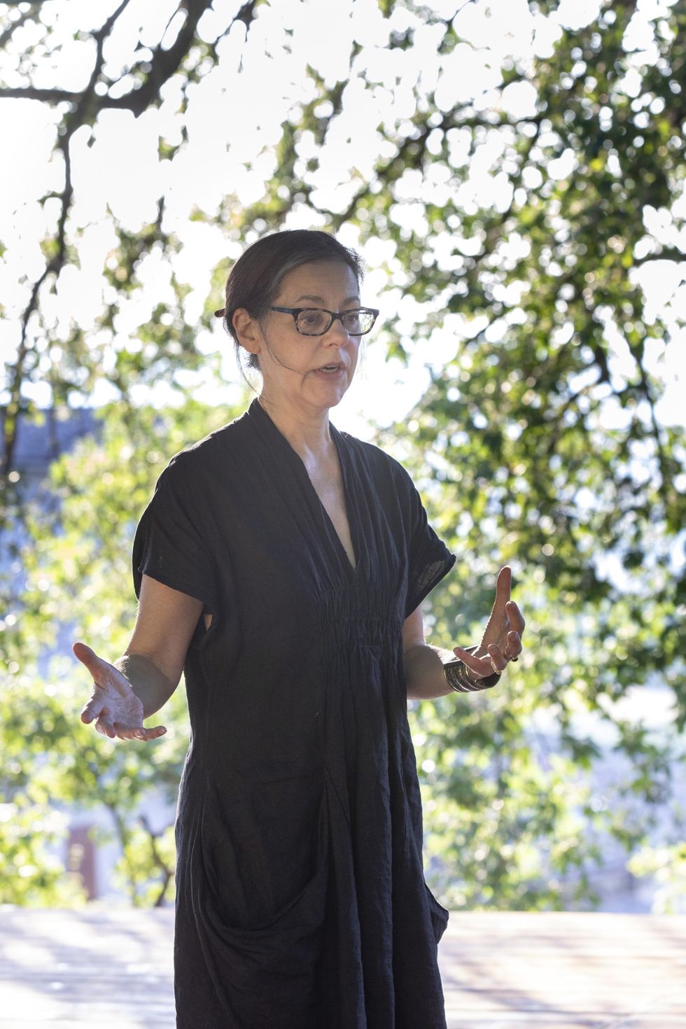 Annie-B Parson gesticulates on a stage with green leaves behind her