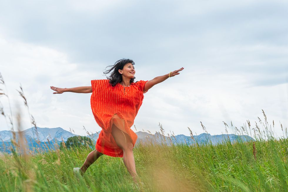 Michelle Boulu00e9 leaps forward in an open field, her red dress swirling around her.