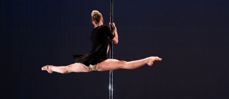 Tekla Kostek holds onto a metal pole in thee dark, her legs open in a horizontal split