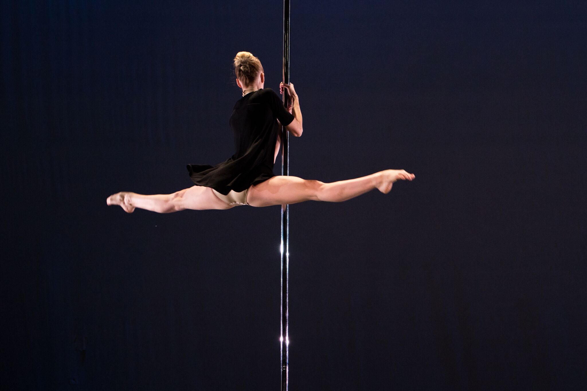 Tekla Kostek holds onto a metal pole in thee dark, her legs open in a horizontal split