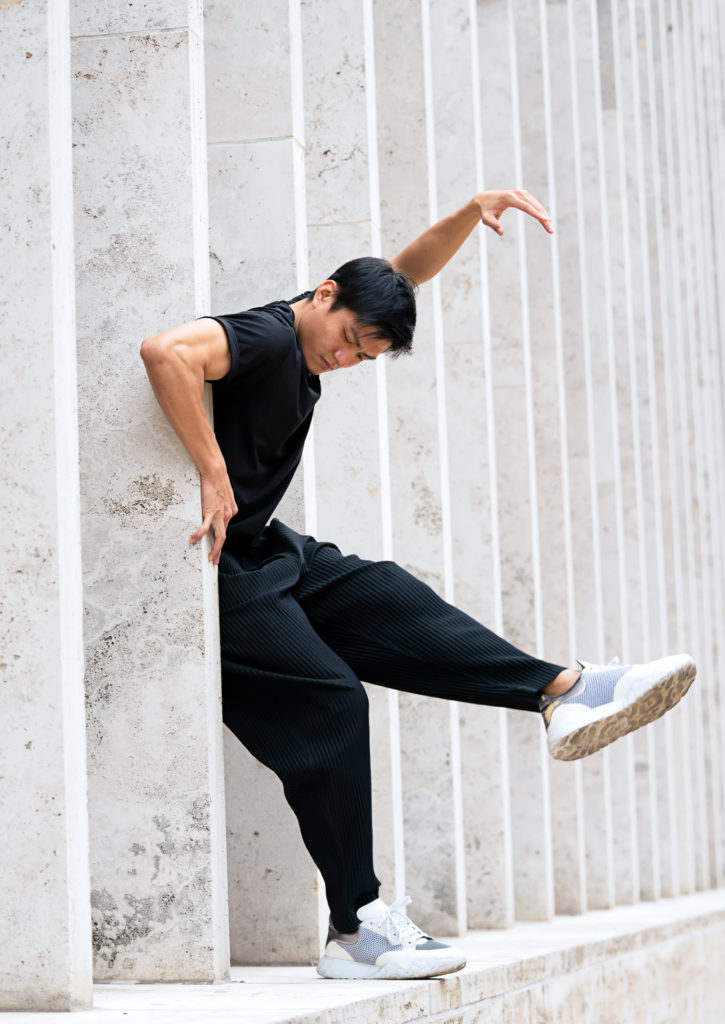 Chun Wai Chan dances in between lage columns, his limbs reaching forward while his hips sink back