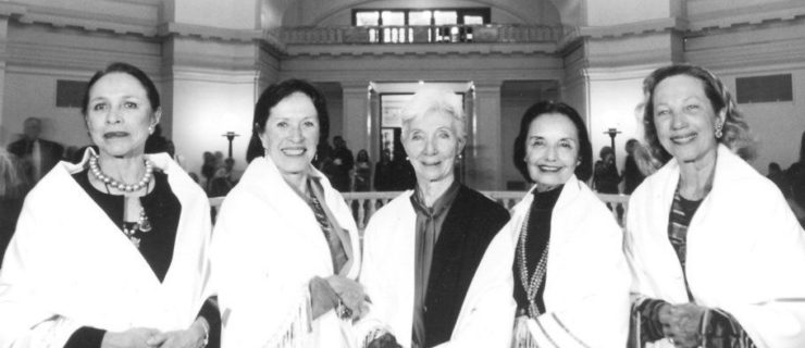 Black and white image of five women standing together with white scarves draped over their shoulders