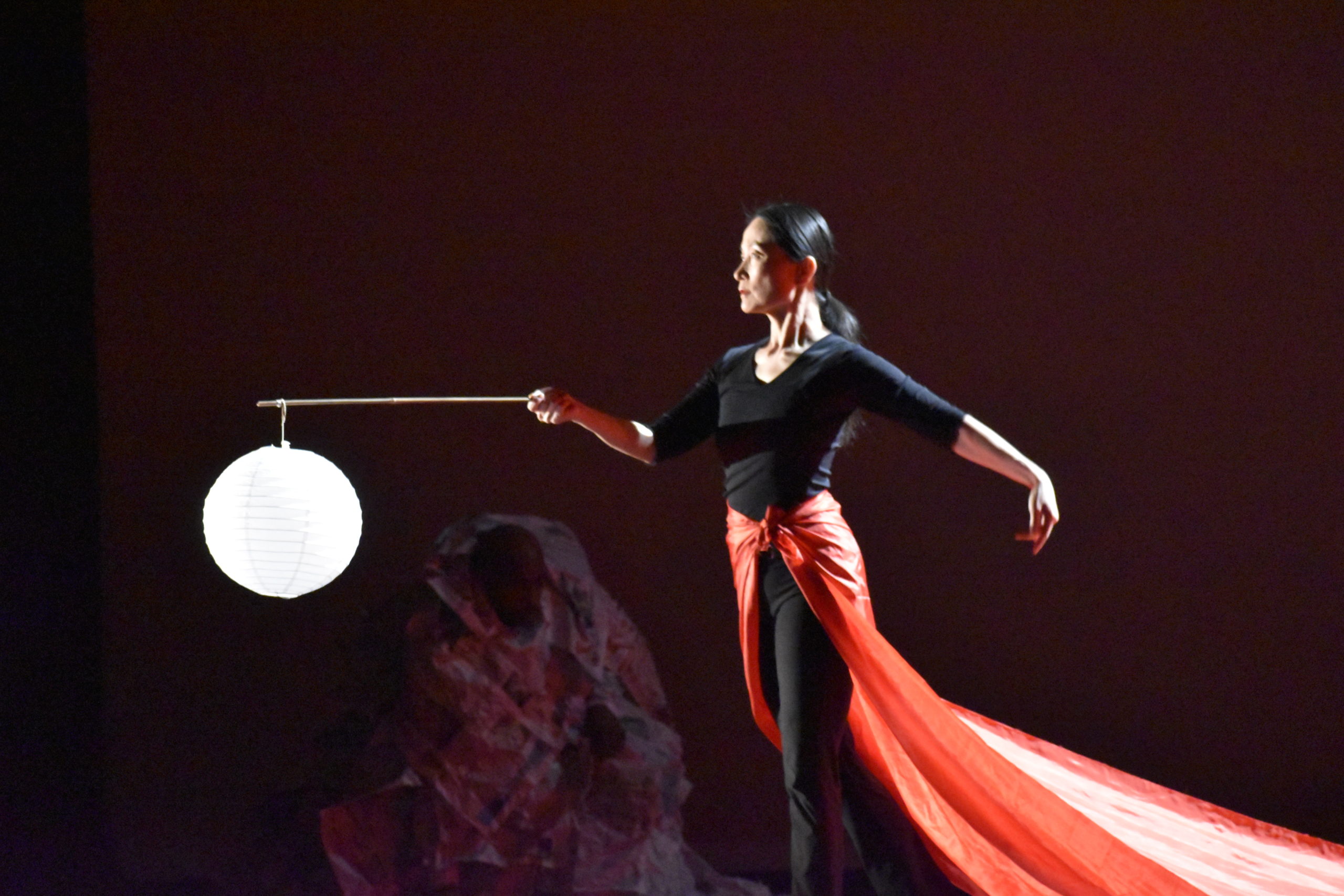 An Asian woman holds a lighted bulb with a long red cape flowing behind her.