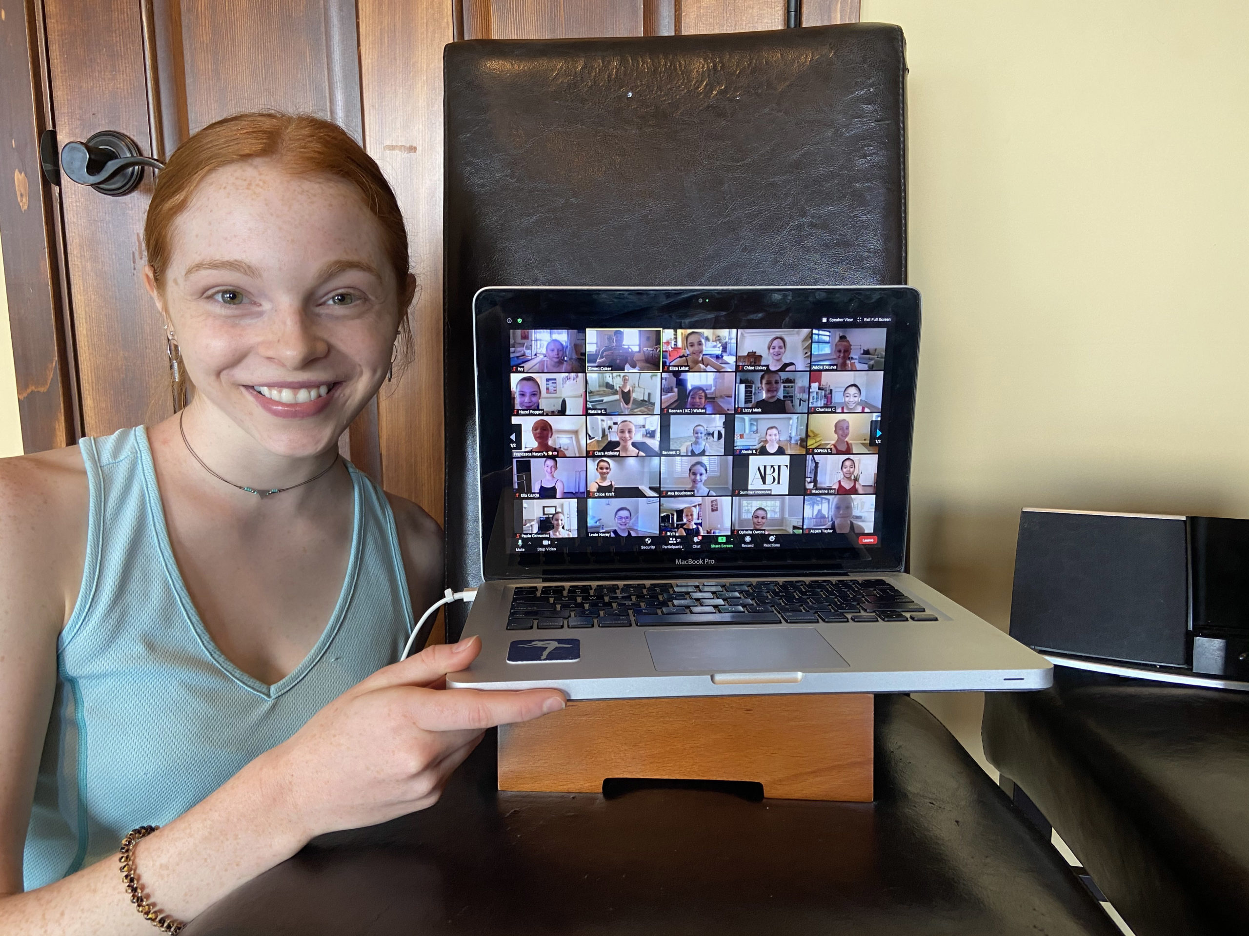 A redhead woman holds up a laptop with the screen showing a Zoom of many screens