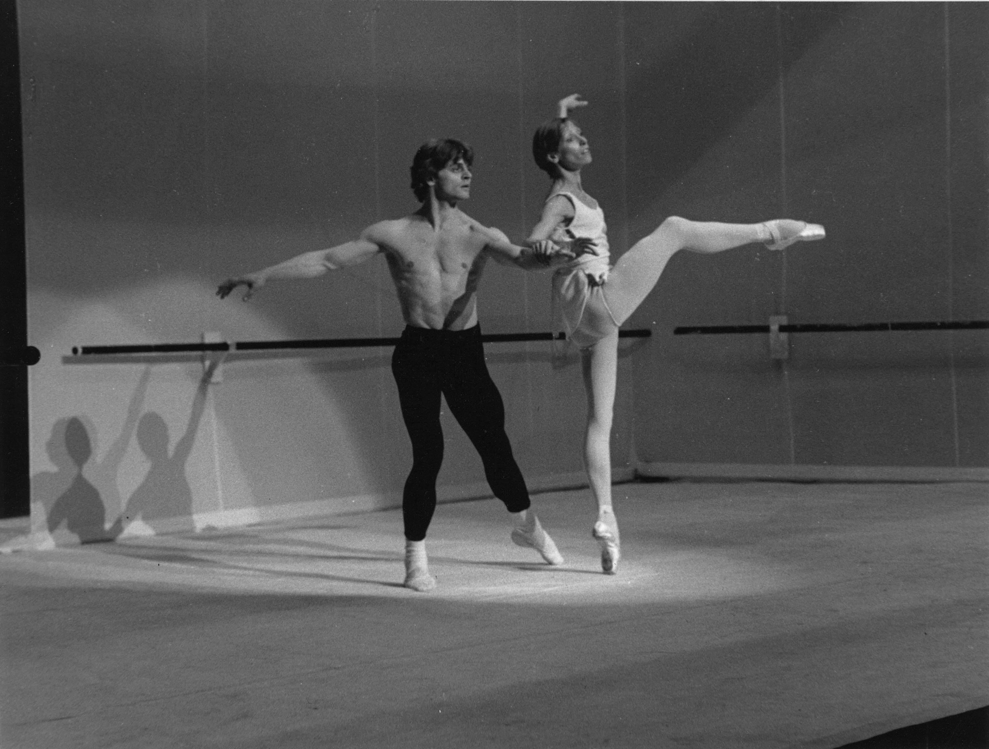 On the set evoking a ballet studio, Baryshnikov supports Makarova with an extended arm as she balances in attitude front. Neither look to each other, but instead out, as though to their reflections in a mirror.