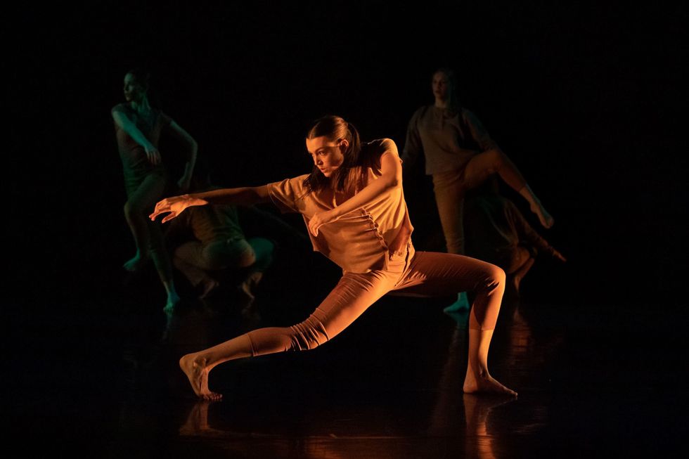 A dancer lit in yellow on a black stages lunges.