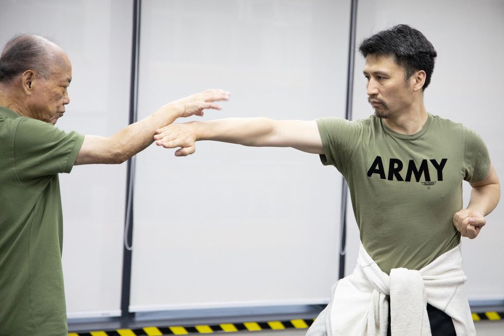 Hong Kong Dance Company Artistic Director Yang Yuntao is in a green shirt. His left fist is clutched by his side, while his right arm shoots out towards his martial arts teacher, also in green.
