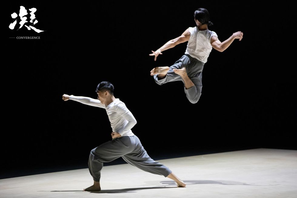 Researcher/dancers Ho Ho-fei on left, and Ong Tze-shen, on right, perform in "Convergence." Ho is in a wide lunge with his right arm punching out and left fist clenched by his side. Ong is in an explosive jump, with legs curled and arms splayed behind her back.