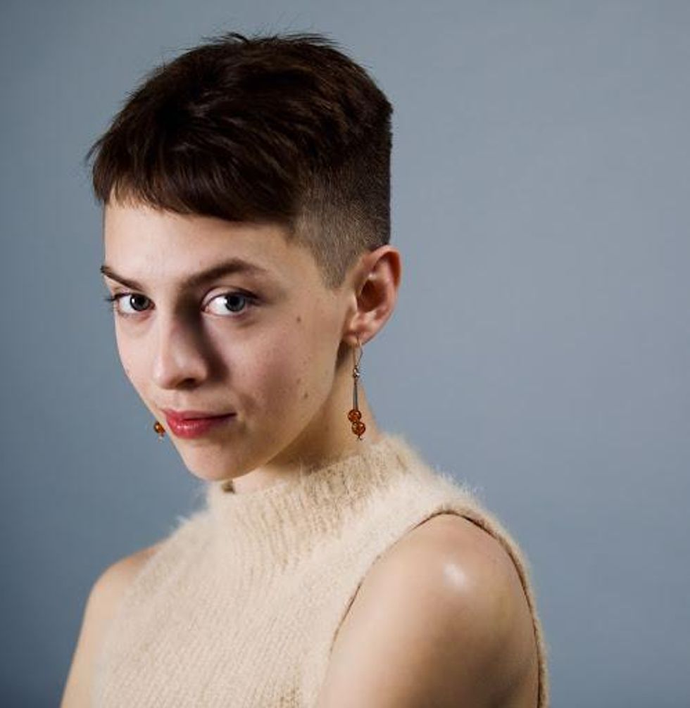Headshot of short-haired brunette looking at the camera, with long earrings and a fuzzy beige tank