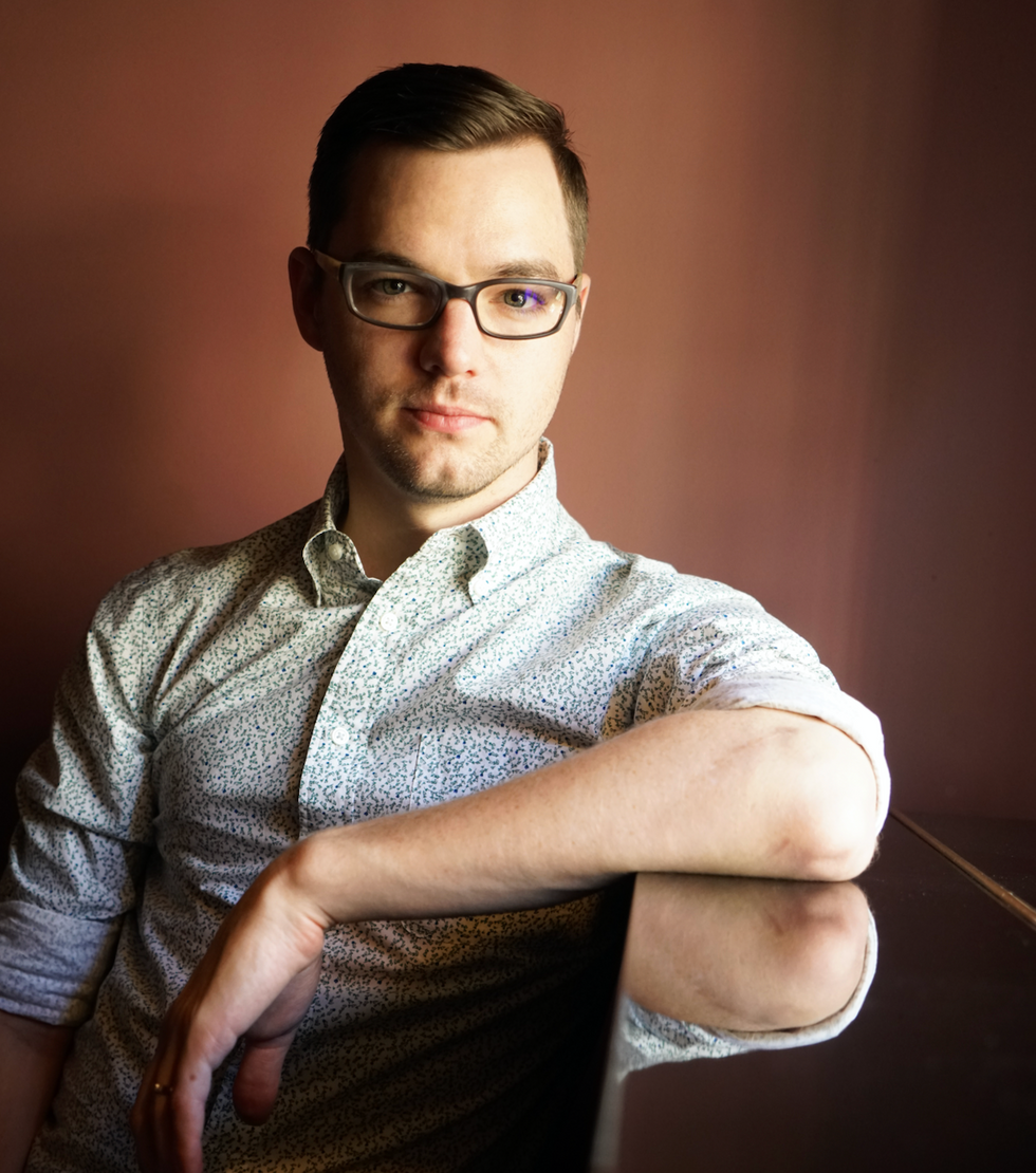 Billy Bell, a white man wearing glasses and a floral button-down shirt, rests his elbow on a table, looking at the camera