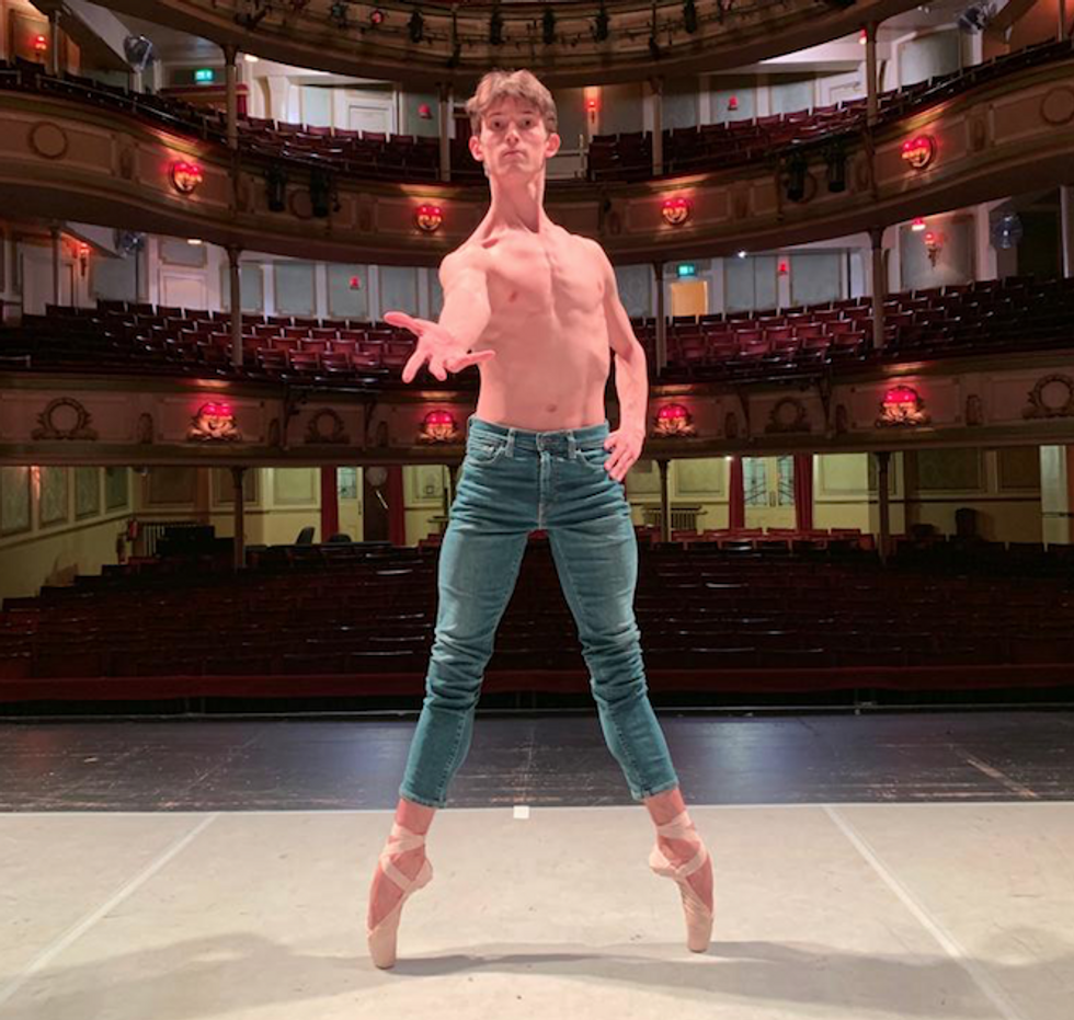 a male ballet dancer poses on a stage in second position on pointe
