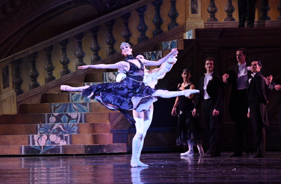 Dancer Jaimi Cullen leaps in a partnered grand jetu00e9 in Nutcracker's party scene, wearing a black dress.