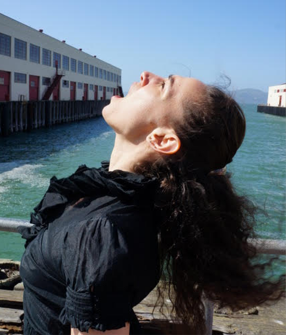 Elswit throws her head back, mouth open in front of a pier
