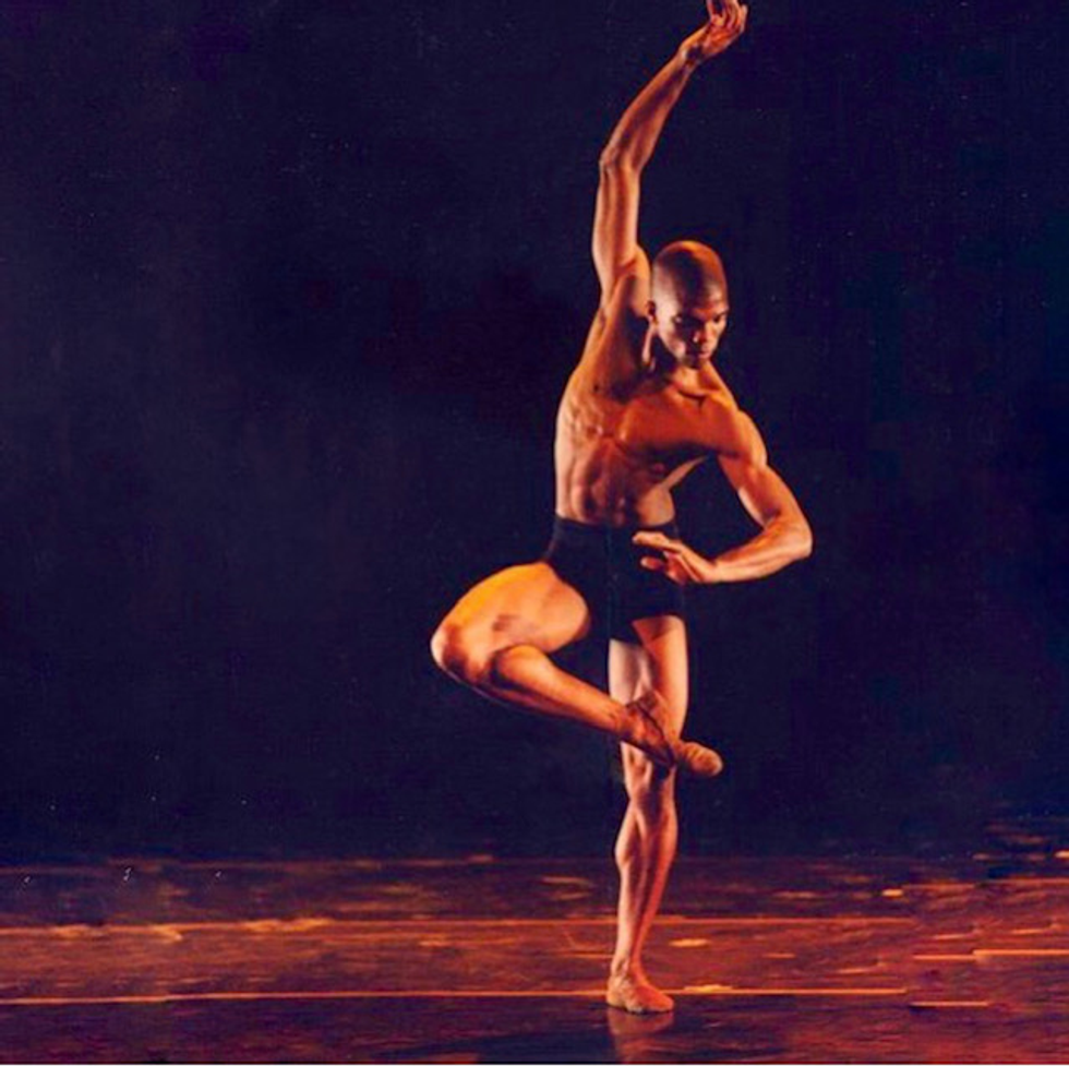 Kevin Boseman stands on one leg on stage, the other ankle crossed at his standing knee, one arm floating up to the sky