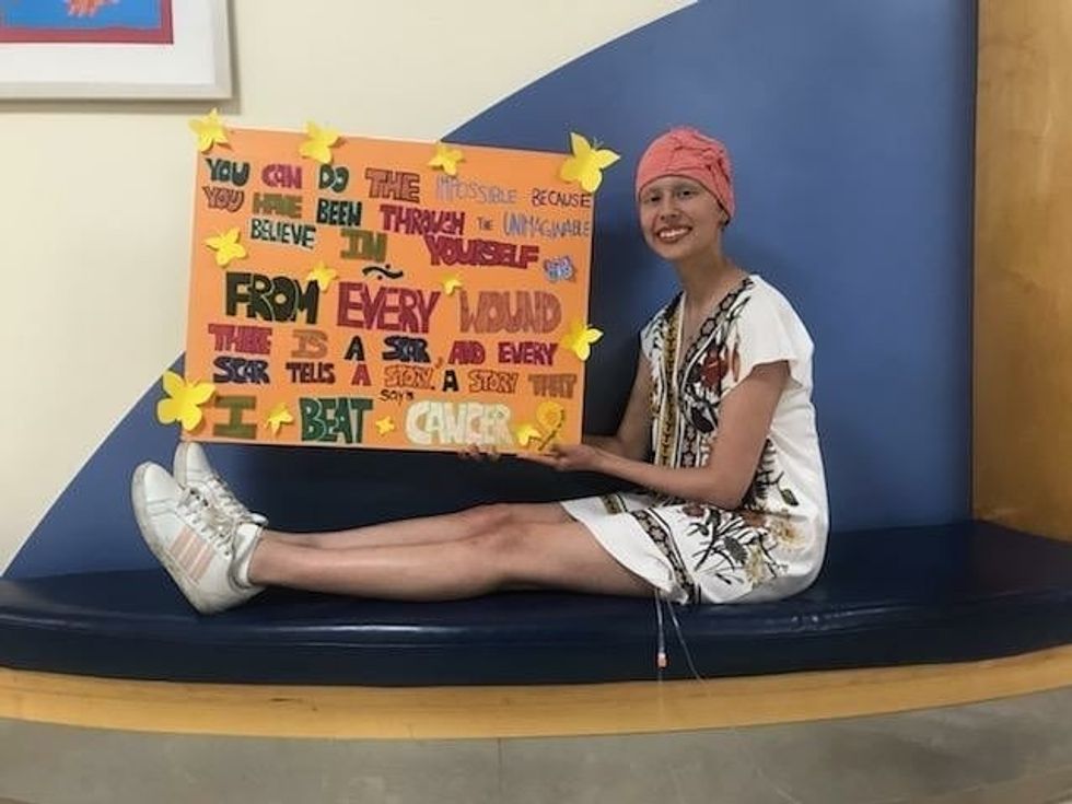 Chiara Valle, on her last day of chemo, shows a poster of inspirational text that ends with, "I beat cancer."