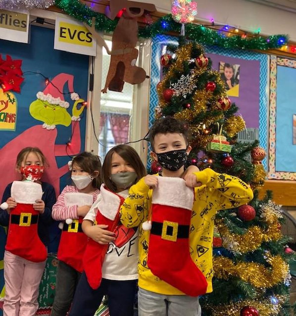 Four children in masks pose with red stockings in front of a Christmas tree.