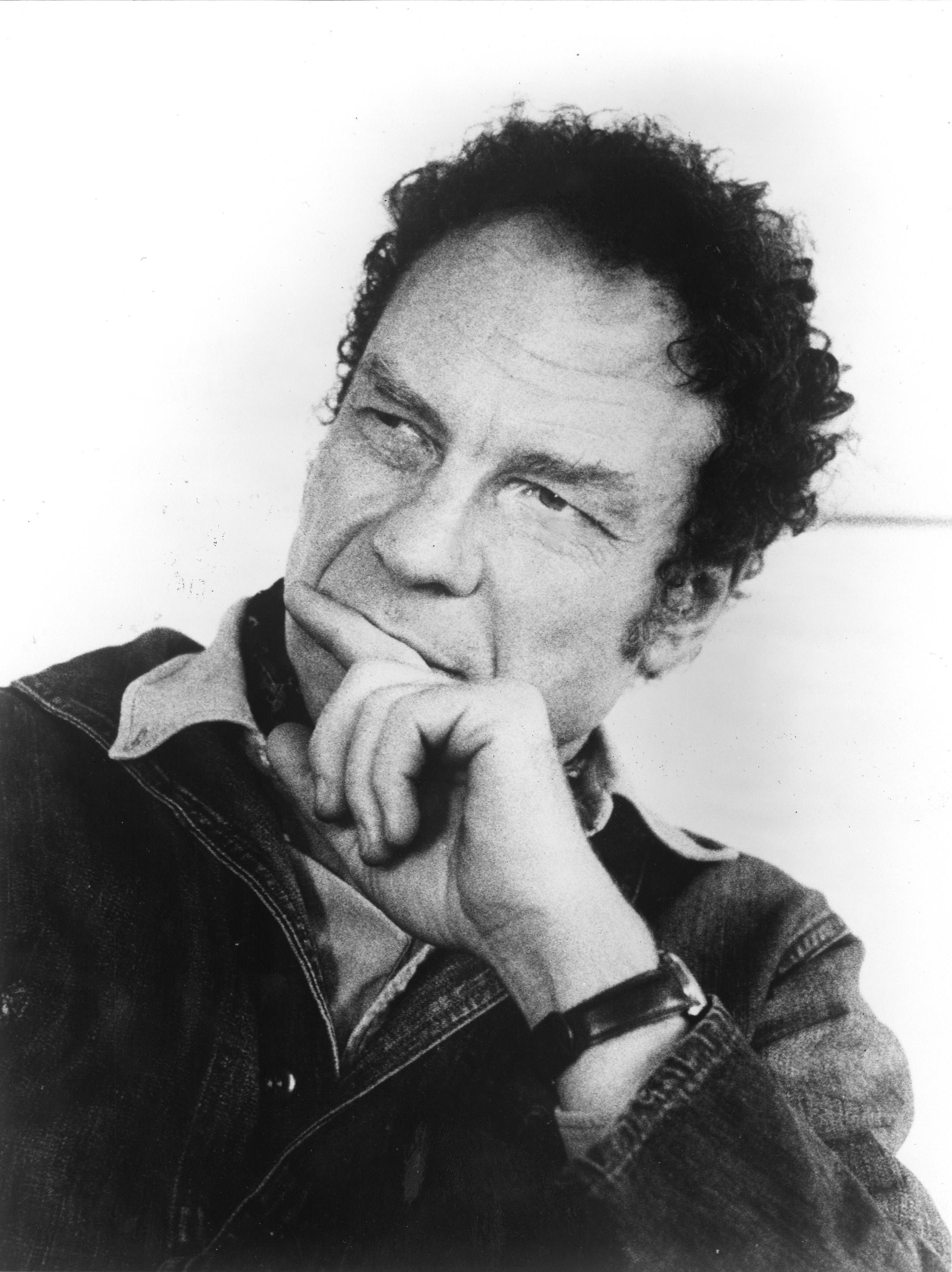 Portrait of a middle-aged Merce Cunningham. His left hand is covering his mouth as he considers something out of frame.