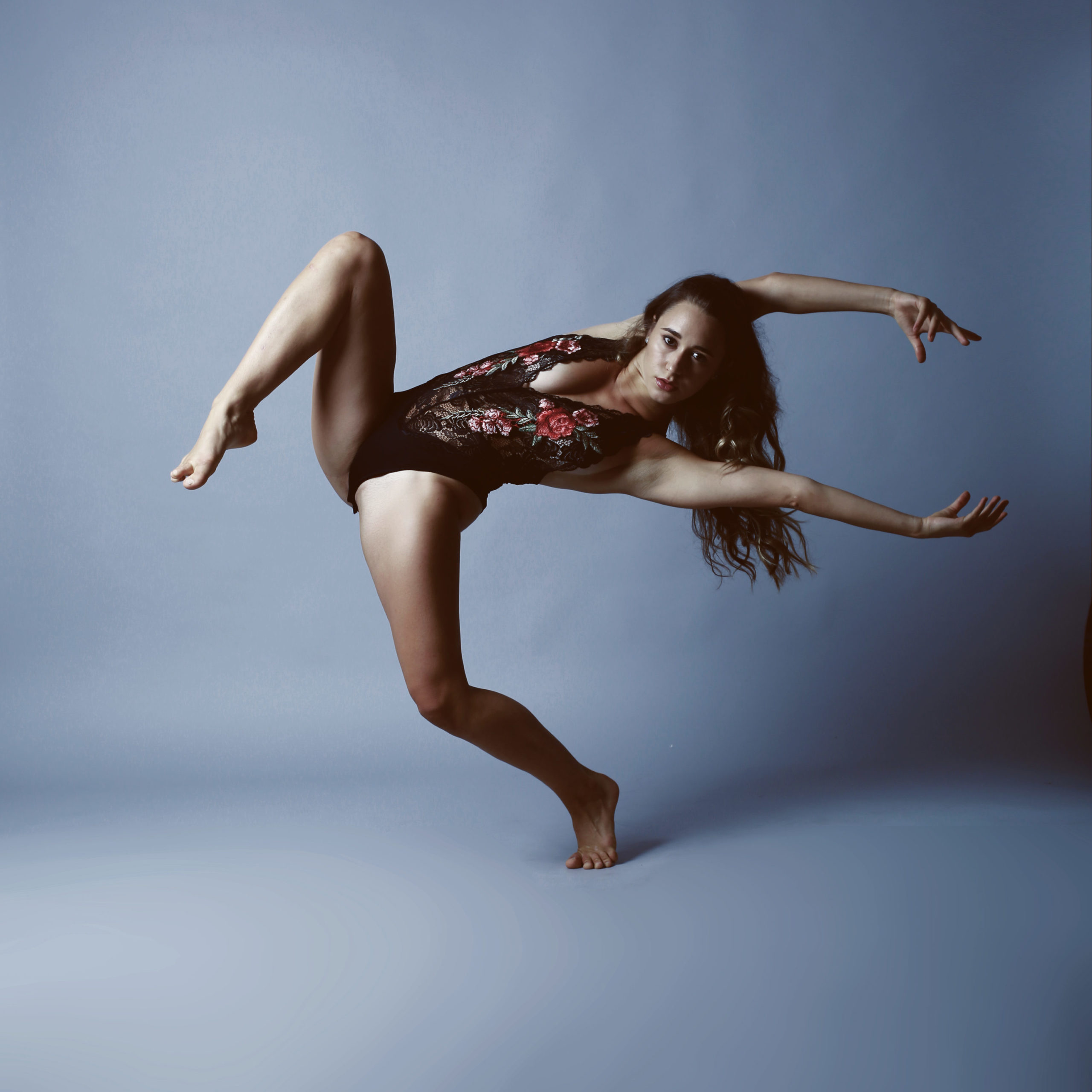 dancer in black floral leotard reaching her arms to the right with one leg up