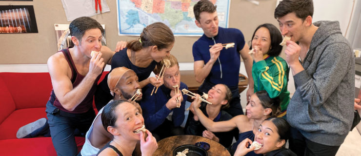 A group of dancers huddle around a table eating dumplings