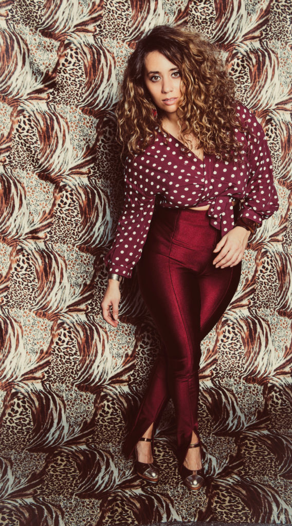 woman with curly brown hair, a red and white polka dot shirt, red pants, and black heels