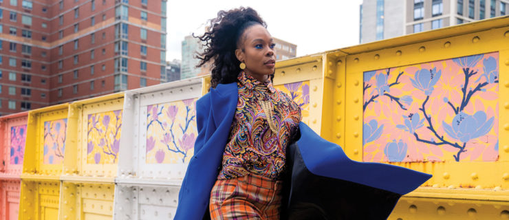 Ebony Williams walks confidently down a city street, blue coat flapping in the wind in from of a yellow structure