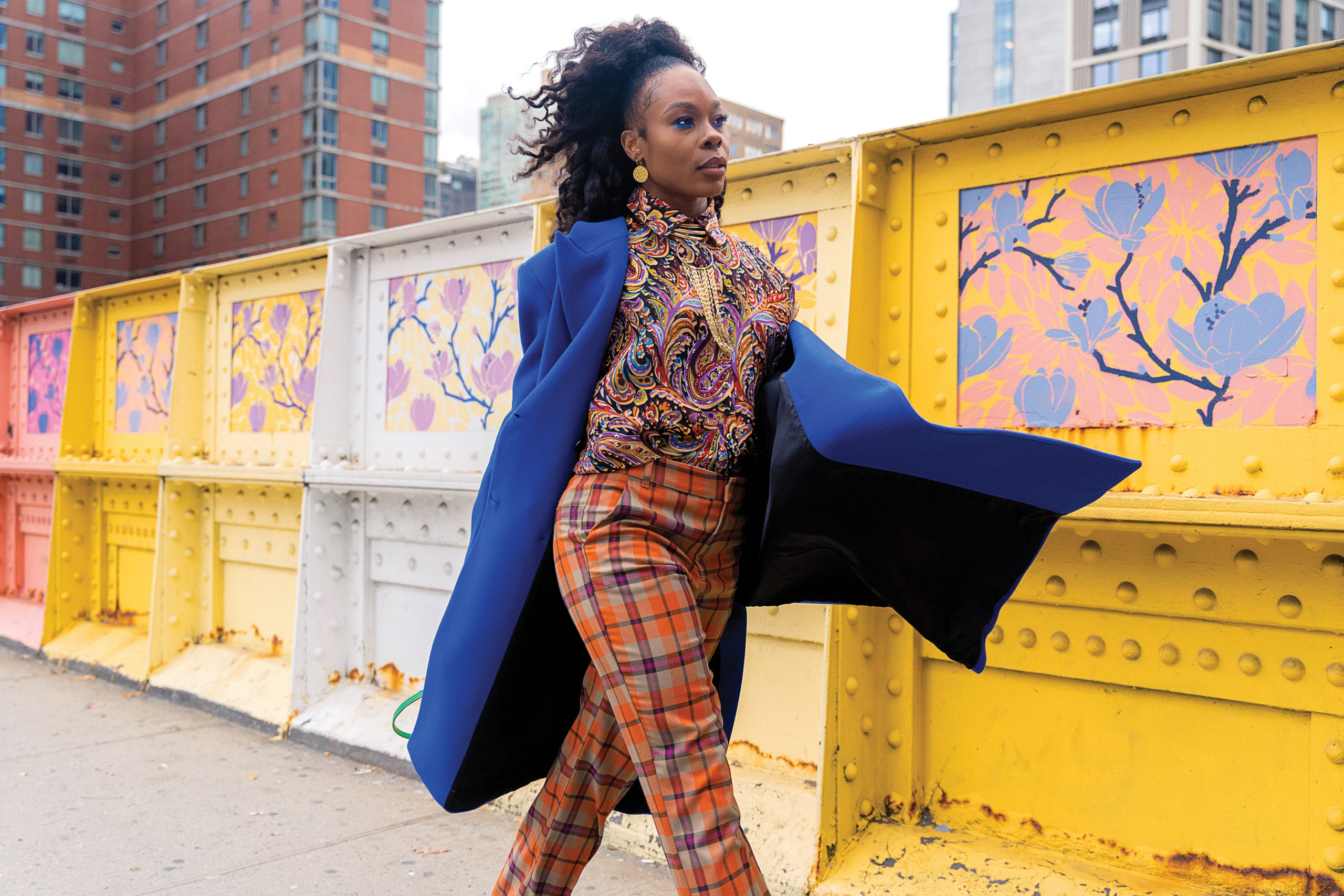 Ebony Williams walks confidently down a city street, blue coat flapping in the wind in from of a yellow structure