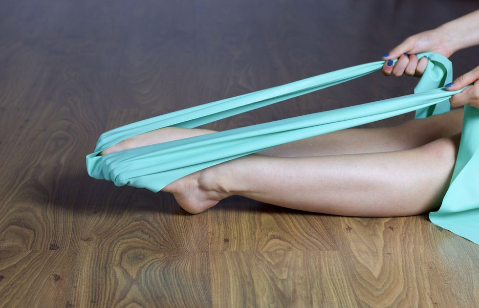 Female legs doing exercises for feet strengthening with elastic band while sitting on wooden floor