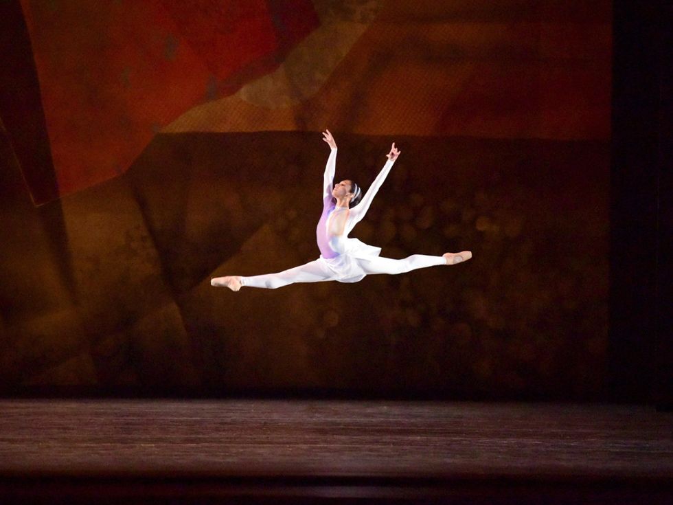 Lall, in white unitard and skirt flies through the air onstage in grand jete