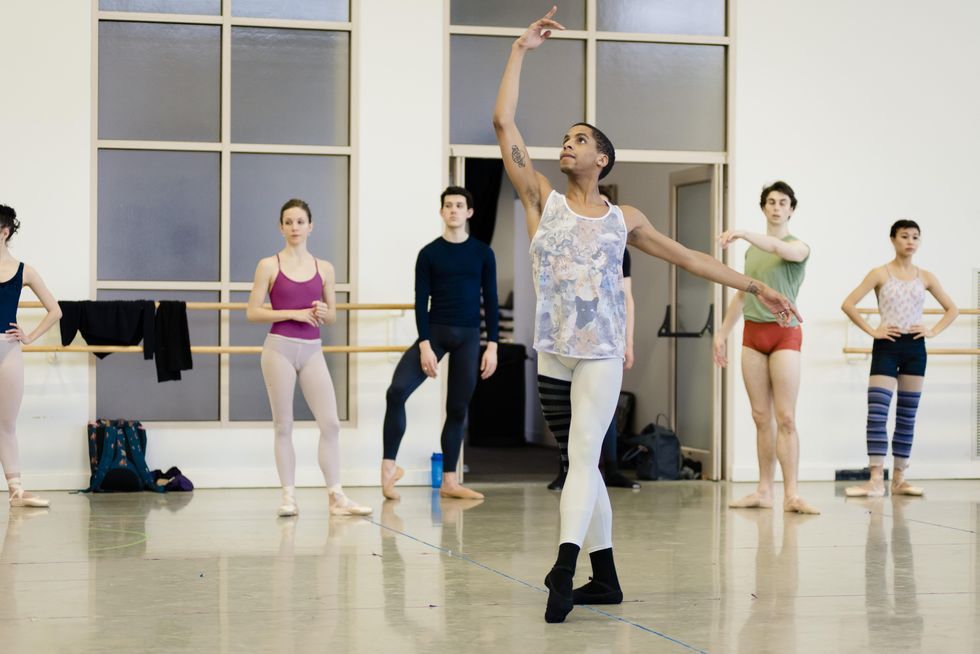 Rines tendus front in a ballet studio with other dancers behind him