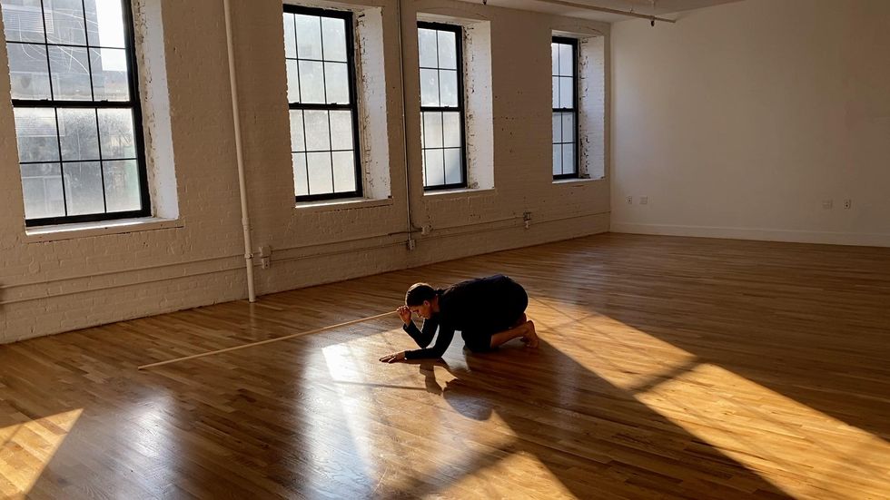 Anna Sperber crouches between rays of sunlight streaming in through windows in an empty studio