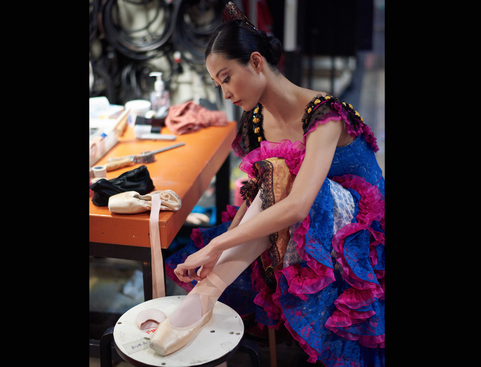 WanTing Zhao ties her pointe shoes on a stool backstage