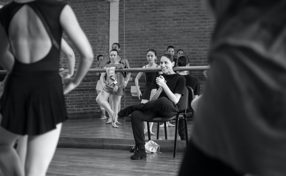 Paloma Herrera sits in a chair in from of a mirror in the ballet studio, smiling at students