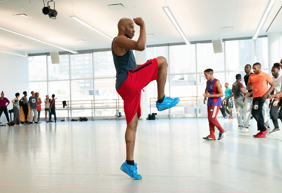 A dancer in rehearsal raises his knee and fist