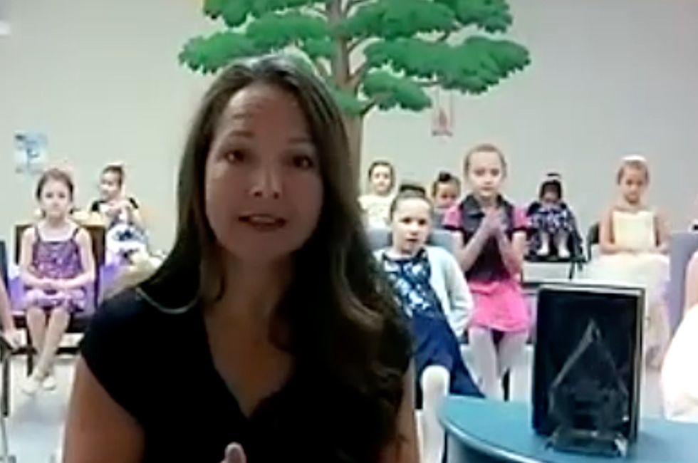 A screenshot of Kim Black accepting her award with a class of students behind her