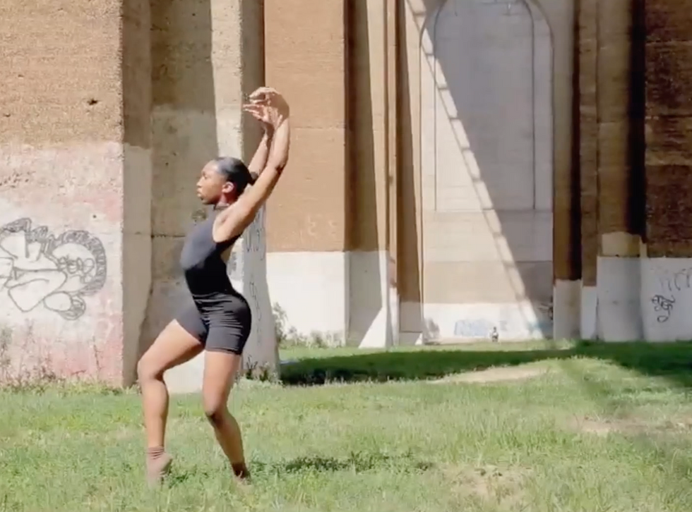 A still from A Prayer for Black Life. Kelsey Lewis wears all black and dances in the grass under a bridge