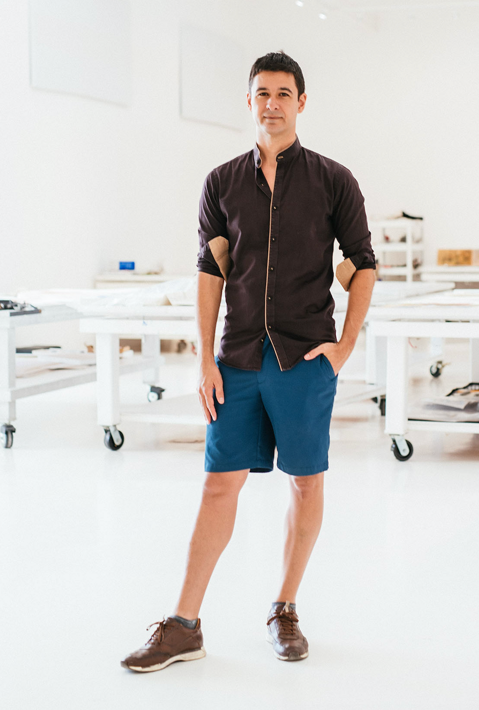 Jonah Bokaer, a brunette man, stands in shorts and long sleeves in front of white tables