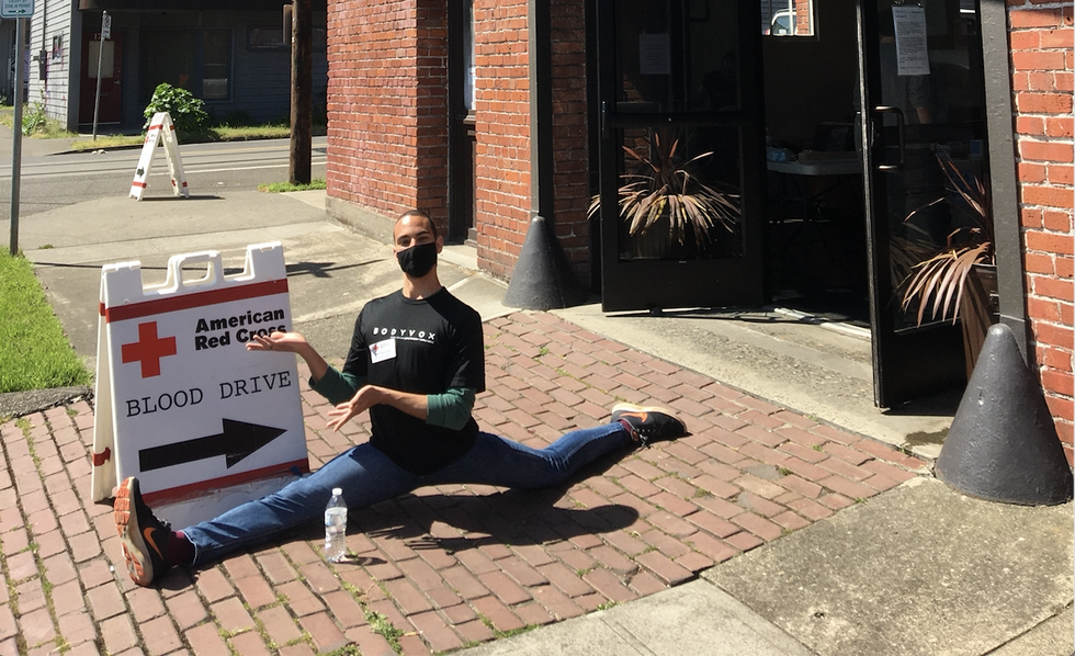 A man splits on a brick sidewalk in jeans in front of a sign pointing to a blood drive.
