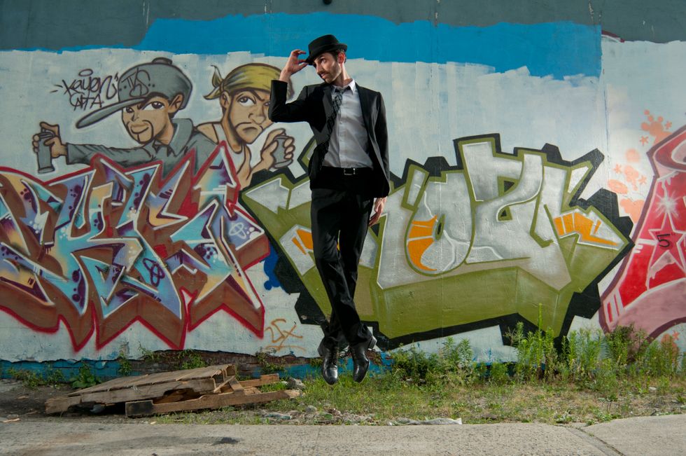 Derek Roland jumps with his feet together in front of a graffitied wall