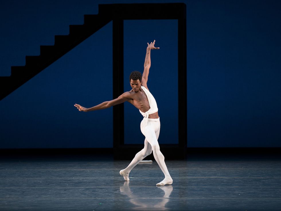 Calvin Royal in all white lunges forward alone on a dark stage