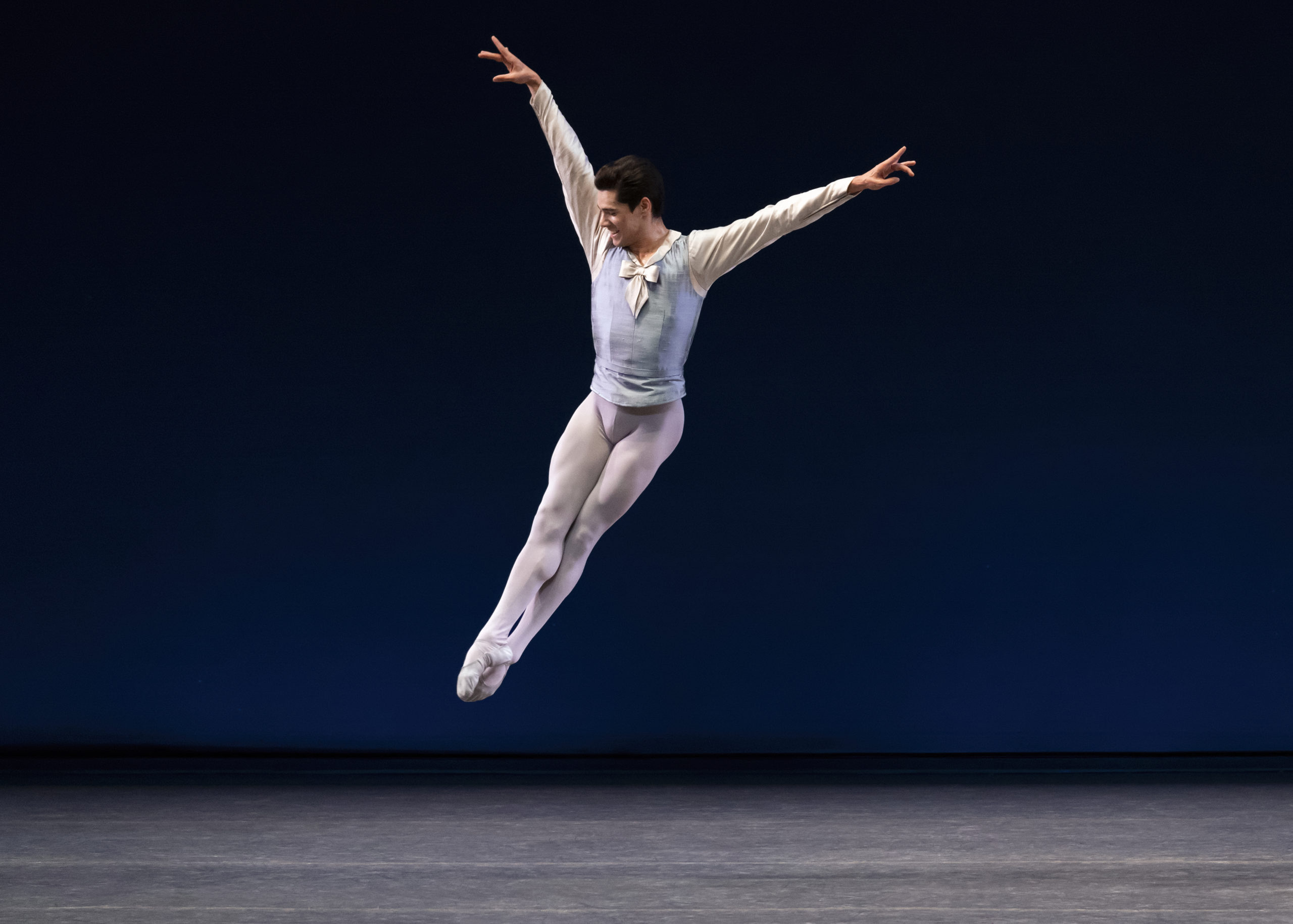 Jovani Furlan, costumed in white tights and ballet slippers and a pale blue tunic, smiles as he soars into an assemblé.