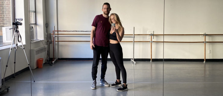 Haley Hilton wears black leggings and tank top, and her husband Coleman Clyde wears a loose maroon short-sleeved T-shirt and dark pants. They have an arm around each other and are taking a selfie in a dance studio, with ballet barres in the background.