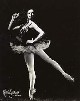 Nina Novak has fair skin and dark hair. She wears a dark tutu and balances in arabesque in pointe shoes.