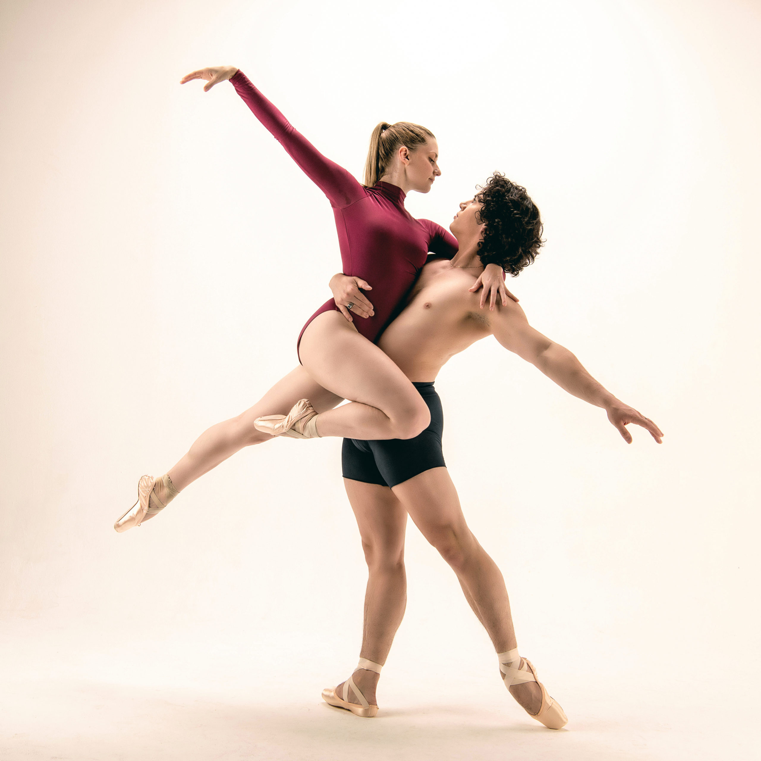 Theresa Knudson is blonde and Roberto Vega Ortiz has dark curly hair. They both wear pointe shoes, and Roberto is lifting Theresa.