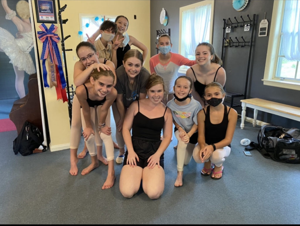 A group of young dancers cluster together in their studio's lobby, smiling at the camera.